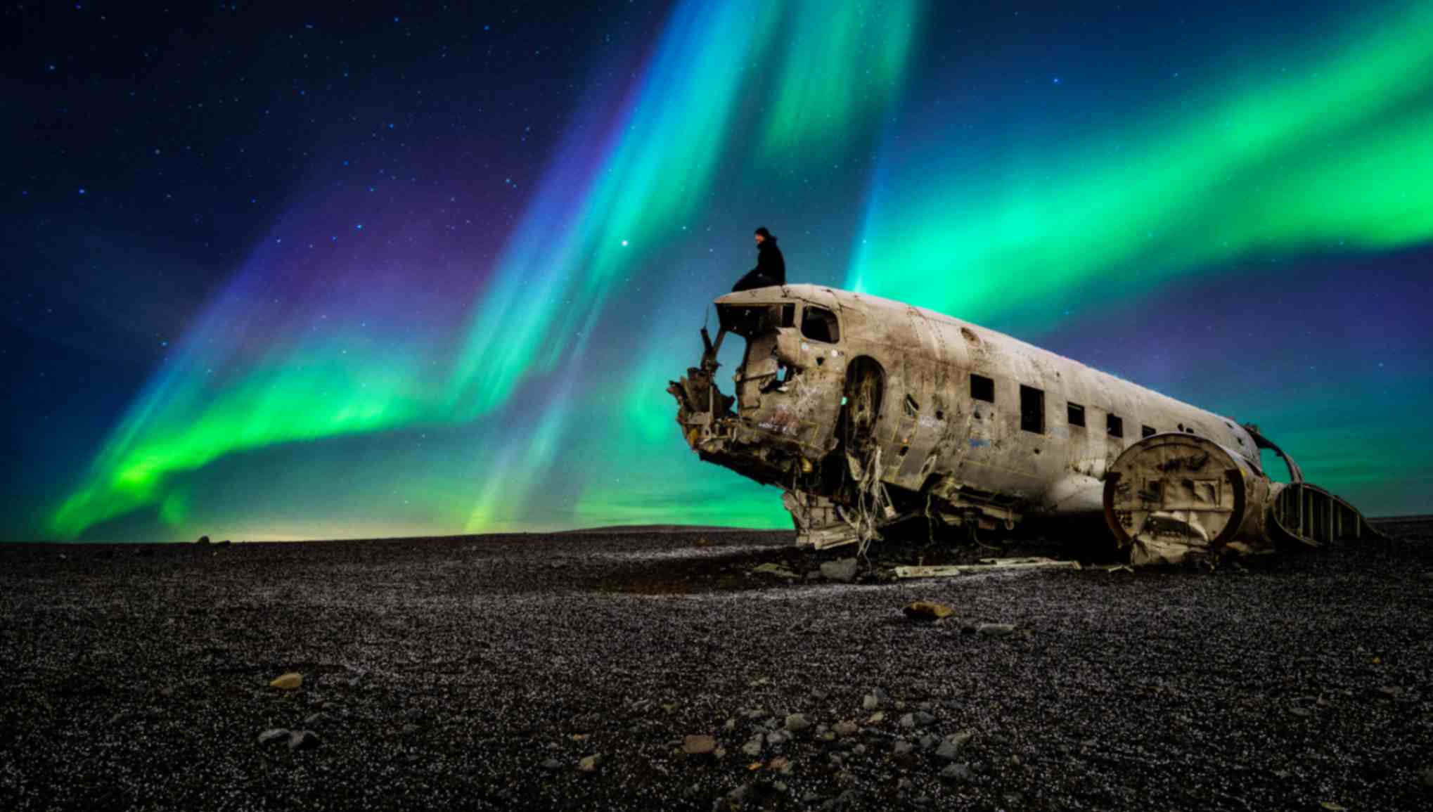 Abandoned plane wreck on black sand beach under northern lights in Iceland