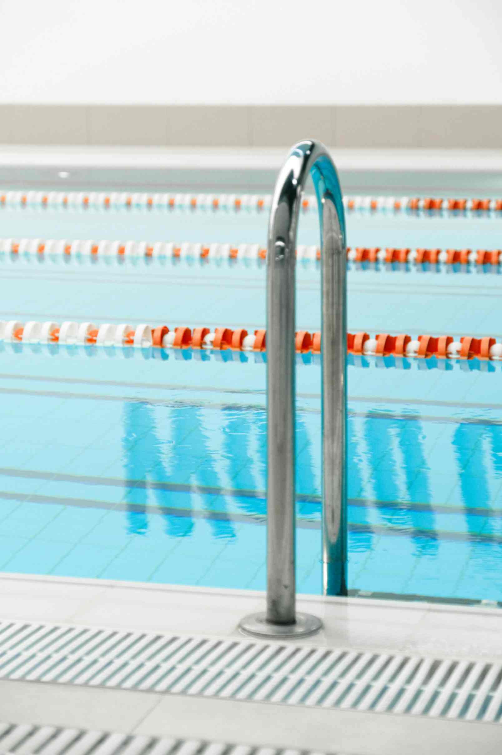 Metal ladder descending into a calm indoor swimming pool with orange-and-white lane dividers.