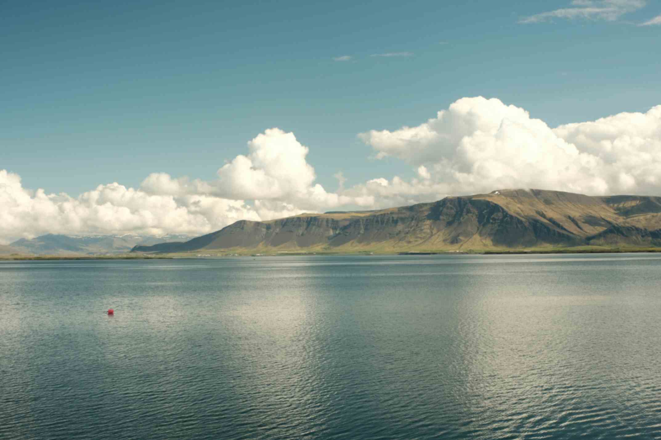 Wide view of a calm bay with mountains in the distance under a partly cloudy sky.
