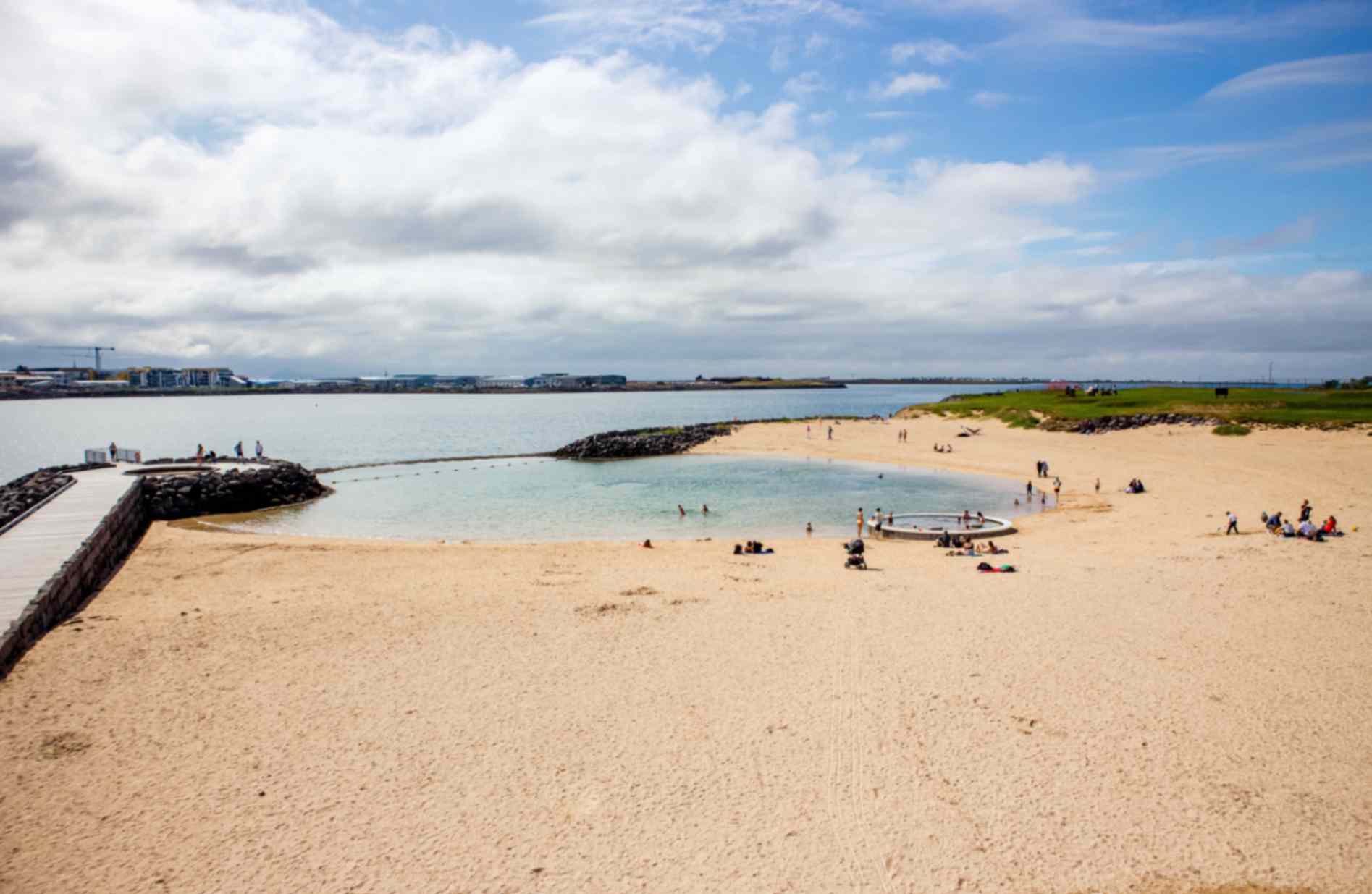 Sandy beach with people relaxing and swimming in a sheltered lagoon by the sea on a bright day.
