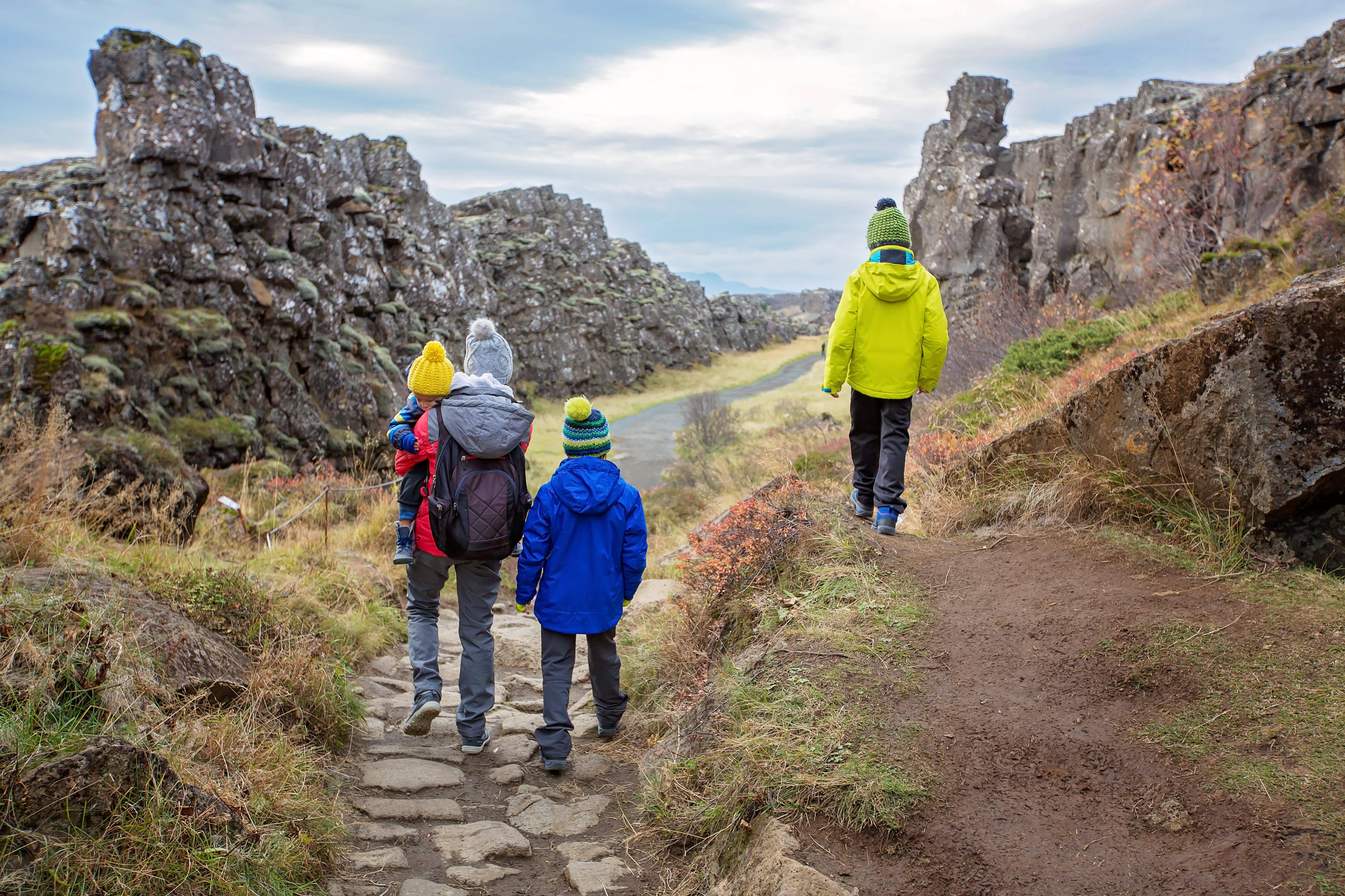 Family walking along a stone path through the Almannagjá gorge in Þingvellir National Park, Iceland, between dramatic volcanic cliffs