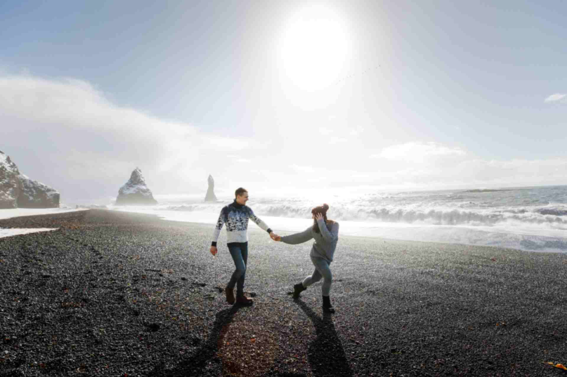 Couple walking on black sand beach with ocean waves in Iceland